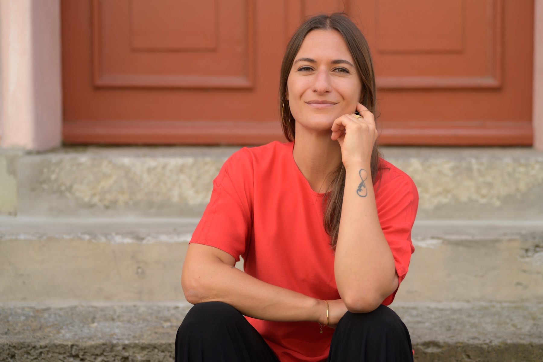 Giulia Barile, systemische Supervisorin und Coach, sitzt in einem roten Shirt auf einer Treppe vor einem Torbogen