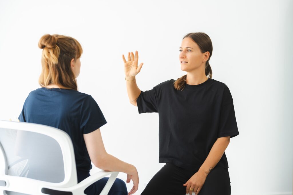 wingwave Coach Giulia Barile, gekleidet in schwarzer Hose und Shirt, erzeugt schnelle rechts-links Augenbewegungen bei ihrer Klientin, indem sie ihre Hand vor den Augen ihrer Klientin schnell hin und her bewegt
