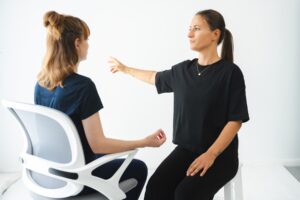 wingwave Coach Giulia Barile, gekleidet in schwarzer Hose und Shirt, erzeugt schnelle rechts-links Augenbewegungen bei ihrer Klientin, indem sie ihre Hand vor den Augen ihrer Klientin schnell hin und her bewegt