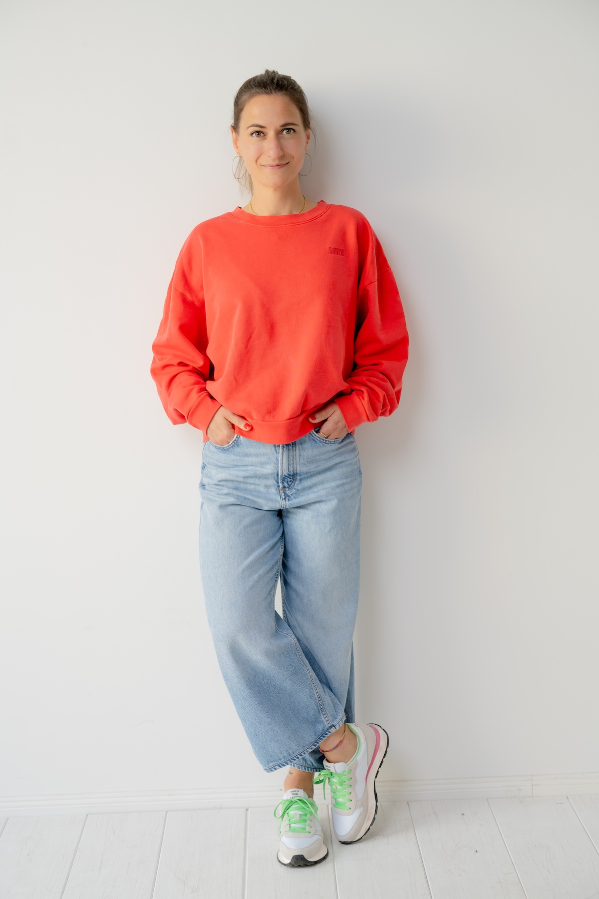 Giulia Barile, DGSv-zertifizierte systemische Supervisorin und Coach und Mentorin für Frauen in der beruflichen Neuorientierung steht an einer weißen Wand, trägt einen roten Pulli, blaue Jeans und weiße Schuhe mit grünen Schnüsenkeln.